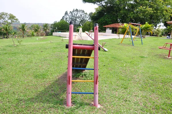 背景木や緑の植生 ブラジル 南米の芝生の上で他のおもちゃと赤と青の色で鉄と木で作られた子供用のスライド — ストック写真