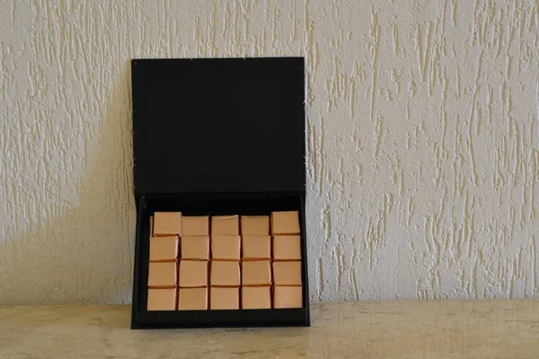 Chocolate. Black box with handmade chocolate bars, wrapped in golden paper, in the background masonry wall, Brazil, South America, zoo photo, copy space on travertine marble table, copy space