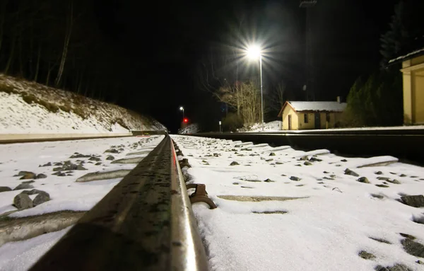 Vista directa desde las vías del tren en una estación de tren nevada por la noche. — Foto de Stock