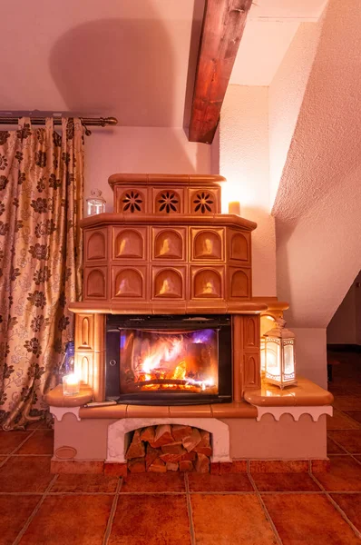 Beige tiled stove in the old style. Ceramic tiles in a cottage, vintage style of interior. Romantic night scenery with fireplace. Front view. Stock Picture