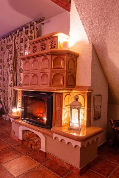 Beige tiled stove in the old style. Ceramic tiles in a cottage, vintage style of interior. Romantic night scenery with fireplace. View from angle. — Stock Photo, Image
