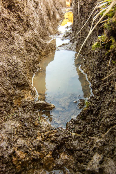 Detalhe de uma escavação cheia de água para colocar tubos de cabo e água após a chuva — Fotografia de Stock