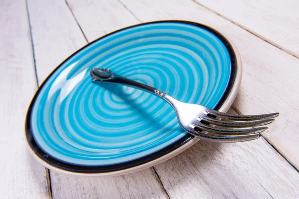 Primo piano di piatto vuoto in ceramica blu, posate in argento antico su tavole di legno bianco anticato vintage. — Foto Stock