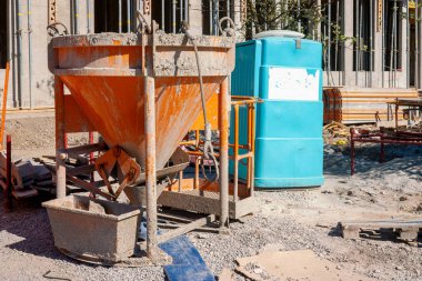 Turuncu beton döken, mavi kiralanabilir tuvaletli, beton takviyeli bir ev için boş inşaat alanı.