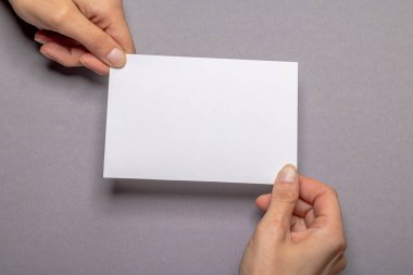 Gri renkli arka plan kartonunun önünde fotokopi alanı olan boş bir kağıt parçasını tutan iki kadın el.
