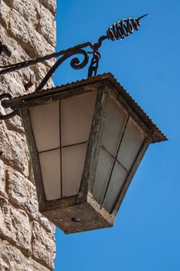 Eski, süslü demir sokak feneri sert bir taş duvarın önünde duruyor güçlü mavi gökyüzünün önünde