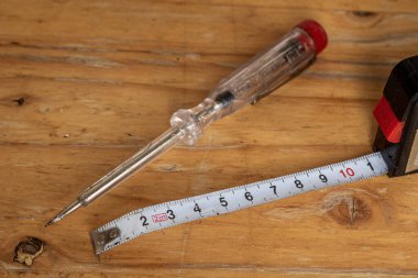Eski voltaj elektrikli test cihazı ve beyaz ölçüm bandı, kendin yap araçları, ahşap bir masanın üzerinde yatıyor.