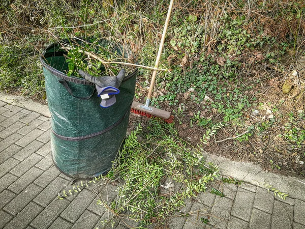 Garden Maintenance work. Green gardener bag and broom. Spring Hedge trimming at fence on a property boundary