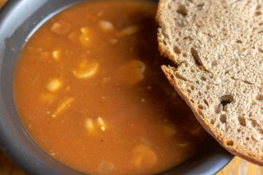 Gulaş çorbası, siyah bir kâse içinde bir dilim gri ekmek ve ahşap bir masa.