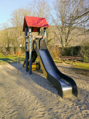 Çocuk parkında kum havuzu ve çatı şeklinde güneş kremi olan modern bir kaydırak.