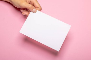 Kadın eli, üzerinde fotokopi alanı olan boş bir kağıt parçasını açık pembe arka plan kartonunun önünde tutuyor.