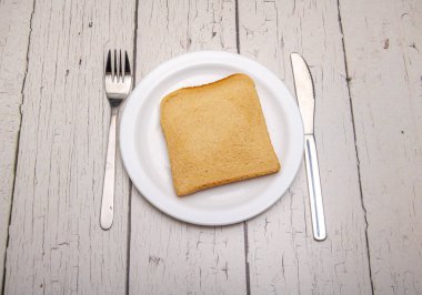 Sade beyaz bir tabakta tek bir dilim tost ve kırsal ahşap bir yüzey üzerinde kullanım belirtileri olan çatal bıçak.