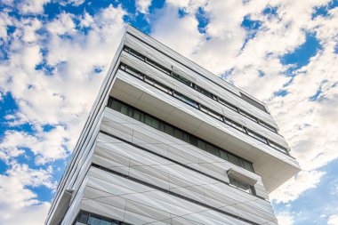 a perspective view of modern building with overhanging upper floors and striking facade against a dramatically lit sky with partial cloud cover