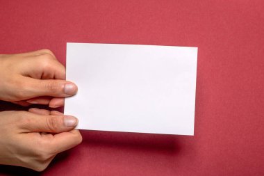 two female hands holding a blank piece of paper with copy space in front of a red background cardboard