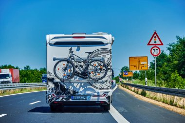 Brandenburg, Almanya - 21 Haziran 2022: Kıça bağlı bir bisiklet taşıyan bir kampçı ve bir kır yolunda üzerine monte edilmiş bir bisiklet.