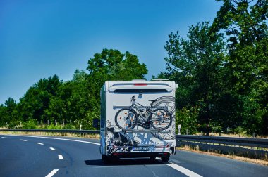 Brandenburg, Almanya - 21 Haziran 2022: Kıça bağlı bir bisiklet taşıyan bir kampçı ve bir kır yolunda üzerine monte edilmiş bir bisiklet.