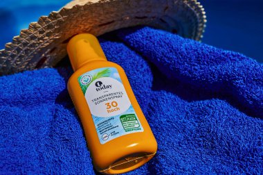 Berlin, Almanya - 24 Temmuz 2022: Yüzme havuzunun yanındaki mavi havluda güneş yanığı önleyici sprey.