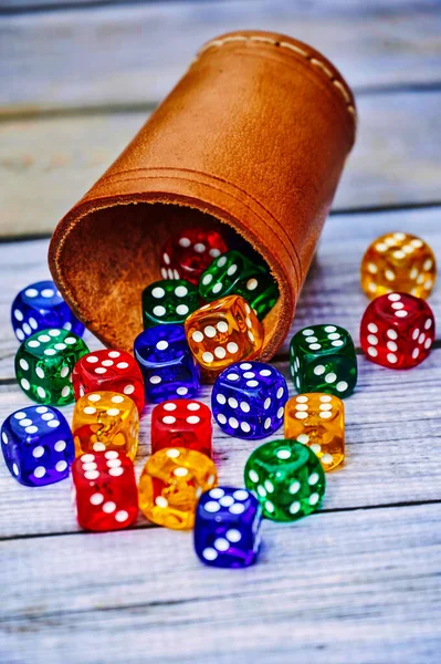 View to different colored game dices and a dice cup on a wooden table.