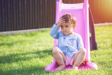 Küçük ve tatlı bir kız kaydırağın üzerinde oynar ve oynarken yüzünü buruşturur..