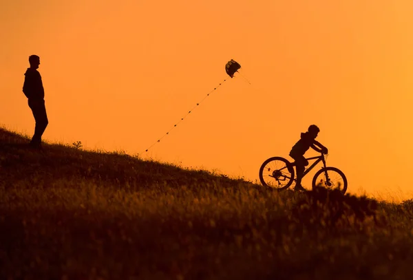 Silhuett Far Och Hans Barn Rida Cykel Med Drake Handen — Stockfoto