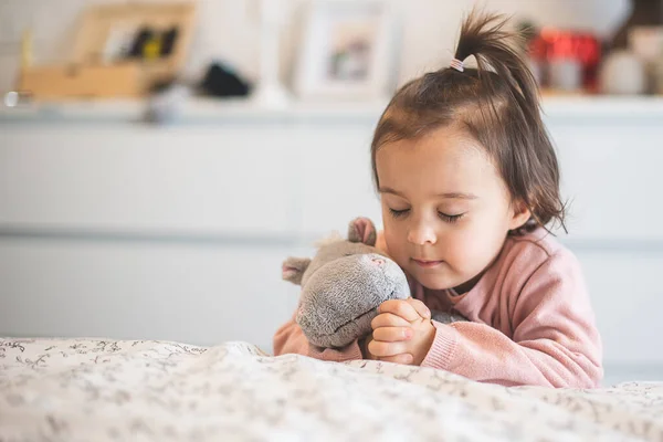 抱着玩具的小女孩在床边祈祷 — 图库照片
