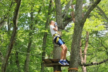 Japanese junior high school student playing zip line at outdoor obstacle course on tree (12 years old)