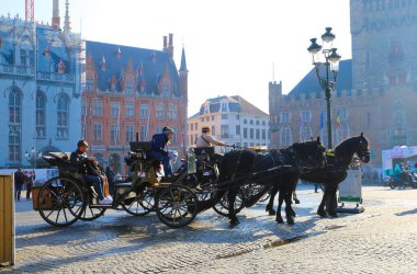 Brugge, Belçika - 9 Ekim. 2021: Görüş alanı için eski at arabası, bulanık ortaçağ binaları arka planı, sabah alacakaranlığı (sol vagona odaklan) ile pazar meydanı (grote markt) görüntüsü)
