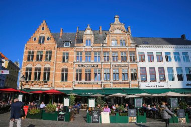 Brugge, Belçika - 9 Ekim. 2021: Güneşli bir sonbahar gününde insanların dışarıda oturduğu ortaçağ evleri ve kafelerle pazar meydanına bakın