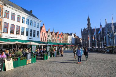 Brugge, Belçika - 9 Ekim. 2021: Pazar meydanında (grote markt) sıcak sonbahar gününde dışarıda oturan insanlarla birlikte kafeler ve restoranlar (ön taraftaki sol binaya odaklanın) görünüm)