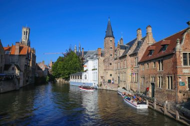Brugge (Rozenhoedkaai), Belçika - 9 Ekim. 2021: Açık mavi gökyüzüne karşı ortaçağ binaları ve gezici teknelerle su kanalına bakın