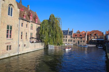 Brugge (Rozenhoedkaai), Belçika - 9 Ekim. 2021: Ortaçağ binaları, yeşil ağaçlar ve açık mavi sonbahar gökyüzüne karşı iskele arkaplanı üzerindeki su kanalına bakın
