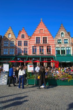 Brugge, Belçika - 9 Ekim. 2021: Yoğun kafeler ve restoranlarla pazar meydanına bakan insanlar, açık mavi sonbahar gökyüzünün dışında oturuyorlar