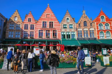 Brugge, Belçika - 9 Ekim. 2021: Yoğun kafeler ve restoranlarla pazar meydanına bakan insanlar, açık mavi sonbahar gökyüzünün dışında oturuyorlar