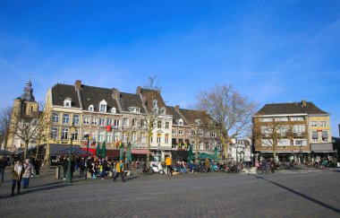 Maastricht, Hollanda - 13 Şubat. 2022: Dışarıdaki restoranlarda mavi kış gökyüzüne karşı insanların oturduğu tipik Hollandalı evlerinin pazar meydanına bakın