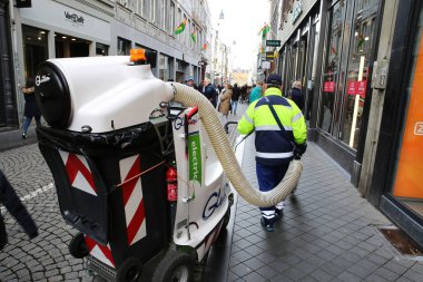 Maastricht, Hollanda - 13 Şubat. 2022: Oburluk vakum temizleme makinesi kullanan kişi ile birlikte halk pedastrian caddesine bakın