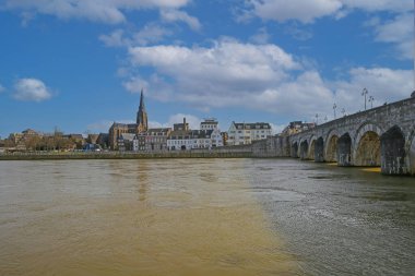 Maastricht (Sint Servaasbrug), Hollanda - 13 Şubat. 2022: Mavi kış gökyüzüne karşı eski kemerli kireçtaşlı yaya köprüsündeki Maas Nehri 'ne bakın