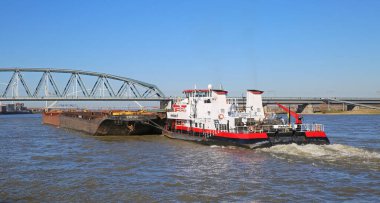 Nijmegen, Hollanda - 27 Şubat. 2022: Mavi gökyüzü ve demiryolu çelik köprüsüne karşı yük mavnası taşıyan HGK satıcı botu Herkül gemisi