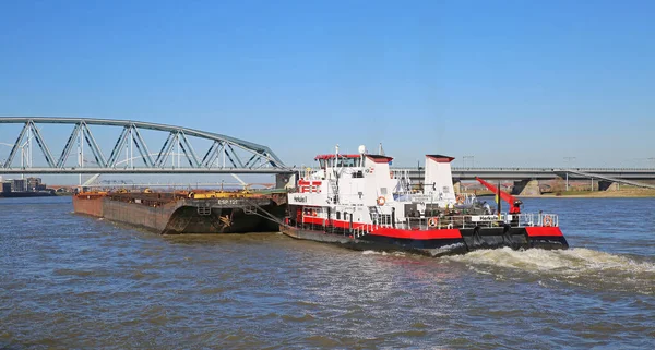 Nijmegen, Hollanda - 27 Şubat. 2022: Mavi gökyüzü ve demiryolu çelik köprüsüne karşı yük mavnası taşıyan HGK satıcı botu Herkül gemisi