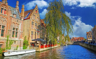 Brugge, Belçika - 9 Ekim. 2021: Deniz kenarındaki bira fabrikası restoranı, yeşil ağaç, mavi gökyüzü, tüylü bulutlar olan ortaçağ eski evlerinde su kanalına bakın