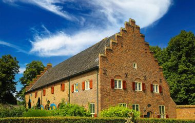 Hollanda 'nın Kasteel Kapısı, Hollanda' da mavi gökyüzüne karşı bahçeli ve yeşil ağaçlı tipik ortaçağ taş evi