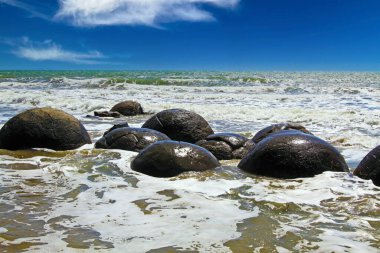 Moeraki Küresel Çamur Taşı 'nın yakınındaki sahilde, Koekohe Sahili, Yeni Zelanda Çakıl Sahili' nde dalgalarla yıkanan kayalar.