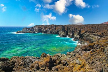 Güzel yalnız göl manzarası, engebeli yaban kayalıkları, turkuaz su dalgaları, mavi gökyüzü - Los Hervidereos, Lanzarote