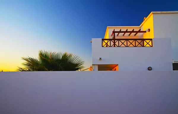 Beautiful white spanish house with terrace, blue sunset sky, ppalm tree, white protection wall - retirement real estate own property concept