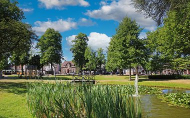 Güzel yeşil Hollanda parkı, gölet, ahşap köprü, mavi yaz gökyüzü bulutları Nuenen, Hollanda