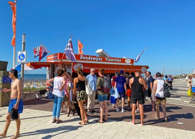 Zandvoort, Netherlands - August 12. 2022: Dutch waterfront promenade with typical fish sale booth, people standing, north sea beach background, blue summer sky