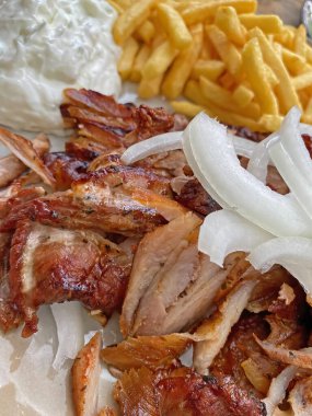 Closeup of isolated ready to eat greek pork gyros plate with onions, french fries and tzatziki dip
