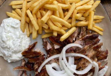 Closeup of isolated ready to eat greek pork gyros plate with onions, french fries and tzatziki dip