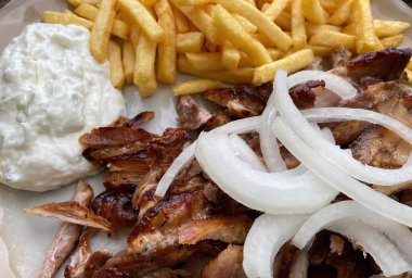 Closeup of isolated ready to eat greek pork gyros plate with onions, french fries and tzatziki dip