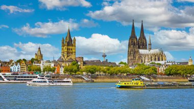 Cologne, Germany - July 9. 2022: Beautiful river rhine waterfront skyline, two churches, dom, cruise ships, blue summer sky fluffy white clouds