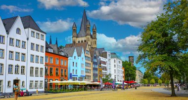 Cologne (Buttermarkt), Germany - July 9. 2022: Beautiful german market square, colorful medieval buildings, St. Martin church tower, blue summer sky fluffy cumulus clouds